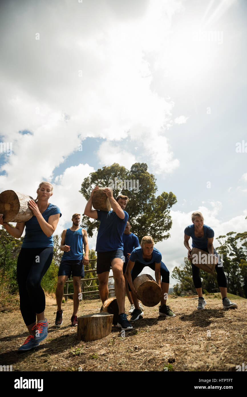 Persone il sollevamento di un carico pesante tronchi di legno durante la corsa a ostacoli in boot camp Foto Stock