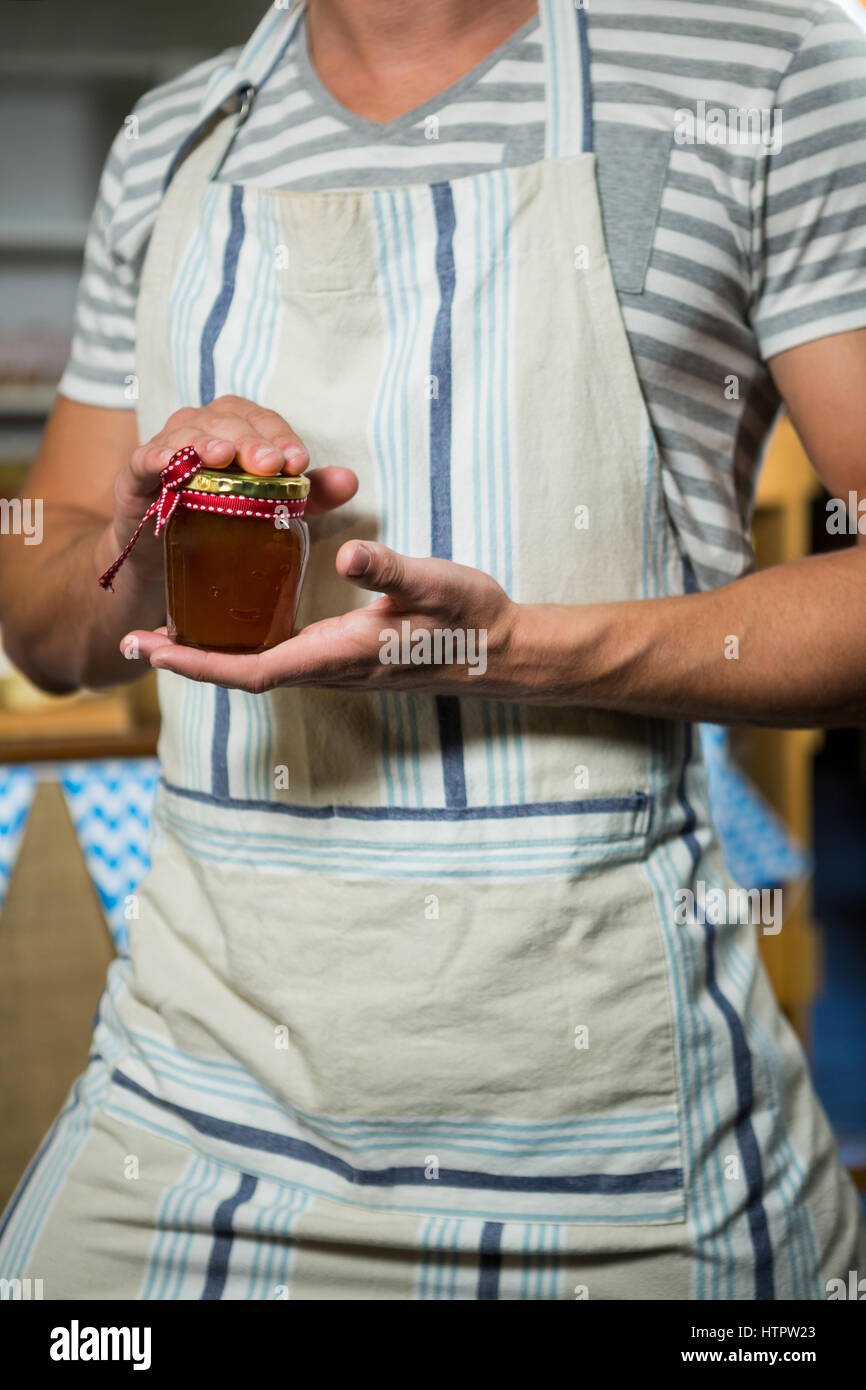 Sezione centrale di un maschio di shop assistant tenendo un vasetto di marmellata Foto Stock