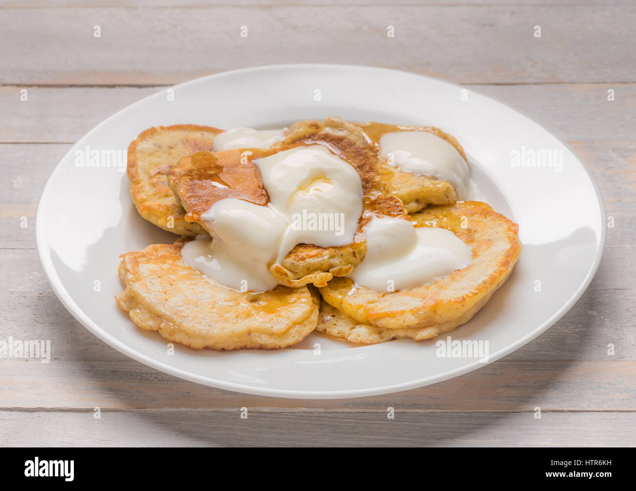 Individuale piccole frittelle di scotch servita su una piastra bianca con yogurt e miele Foto Stock