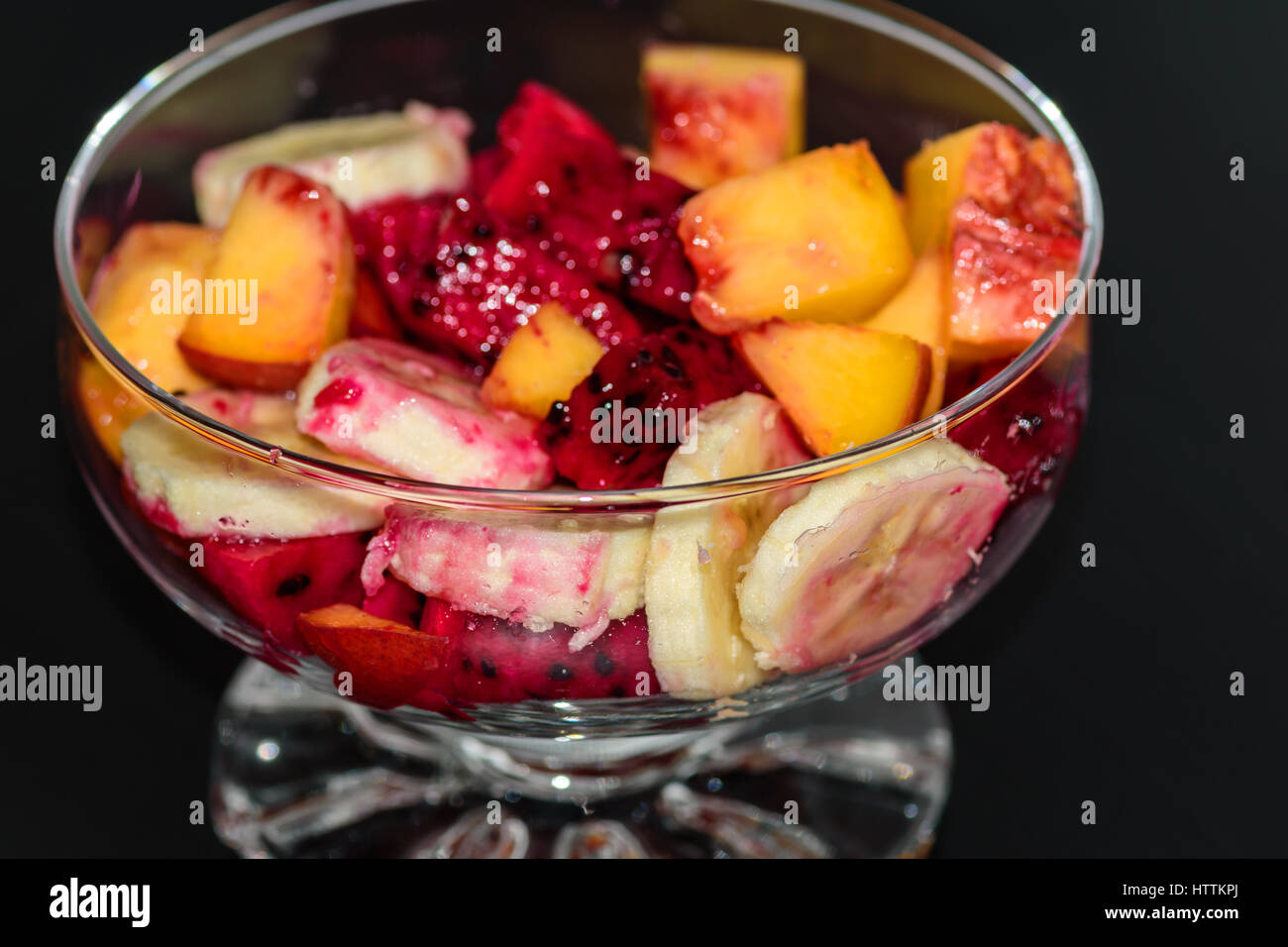 Insalata di frutta su sfondo scuro, pesche, banana, frutto del drago Foto Stock