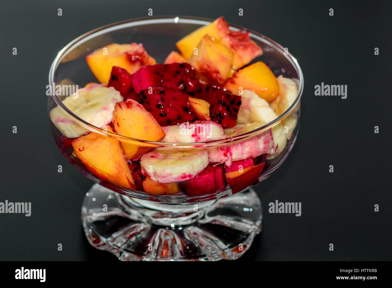 Insalata di frutta su sfondo scuro, pesche, banana, frutto del drago Foto Stock