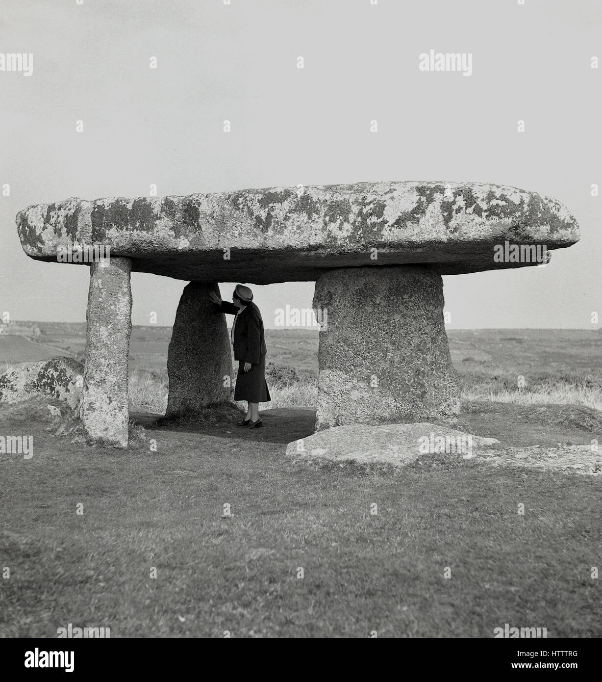 Degli anni Cinquanta, storico, donna sorge sotto la antica struttura in pietra o dolmen, Lanyon Quoit, Morvah. Cornovaglia, Inghilterra. Foto Stock