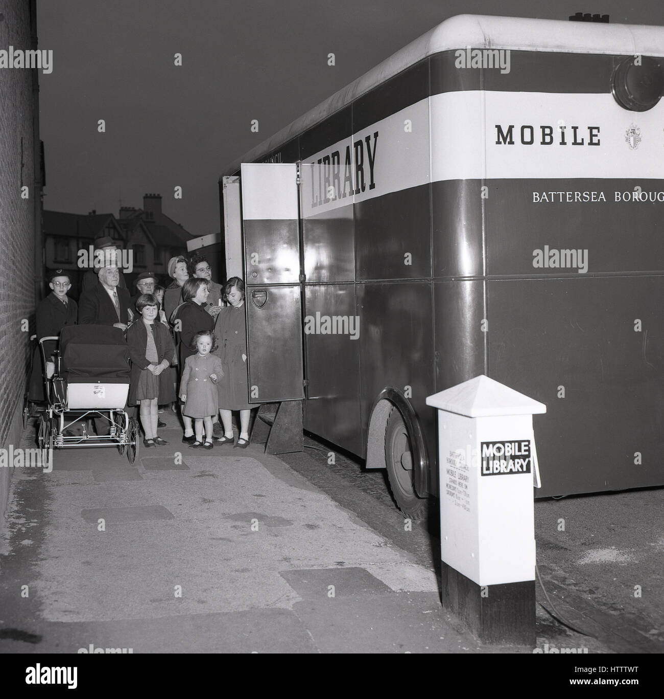 Anni '50, storici, adulti, bambini e una madre con un pRAM in piedi su un marciapiede fuori una biblioteca mobile che sta visitando la loro proprietà immobiliare, Battersea, Londra del sud, Inghilterra. Foto Stock