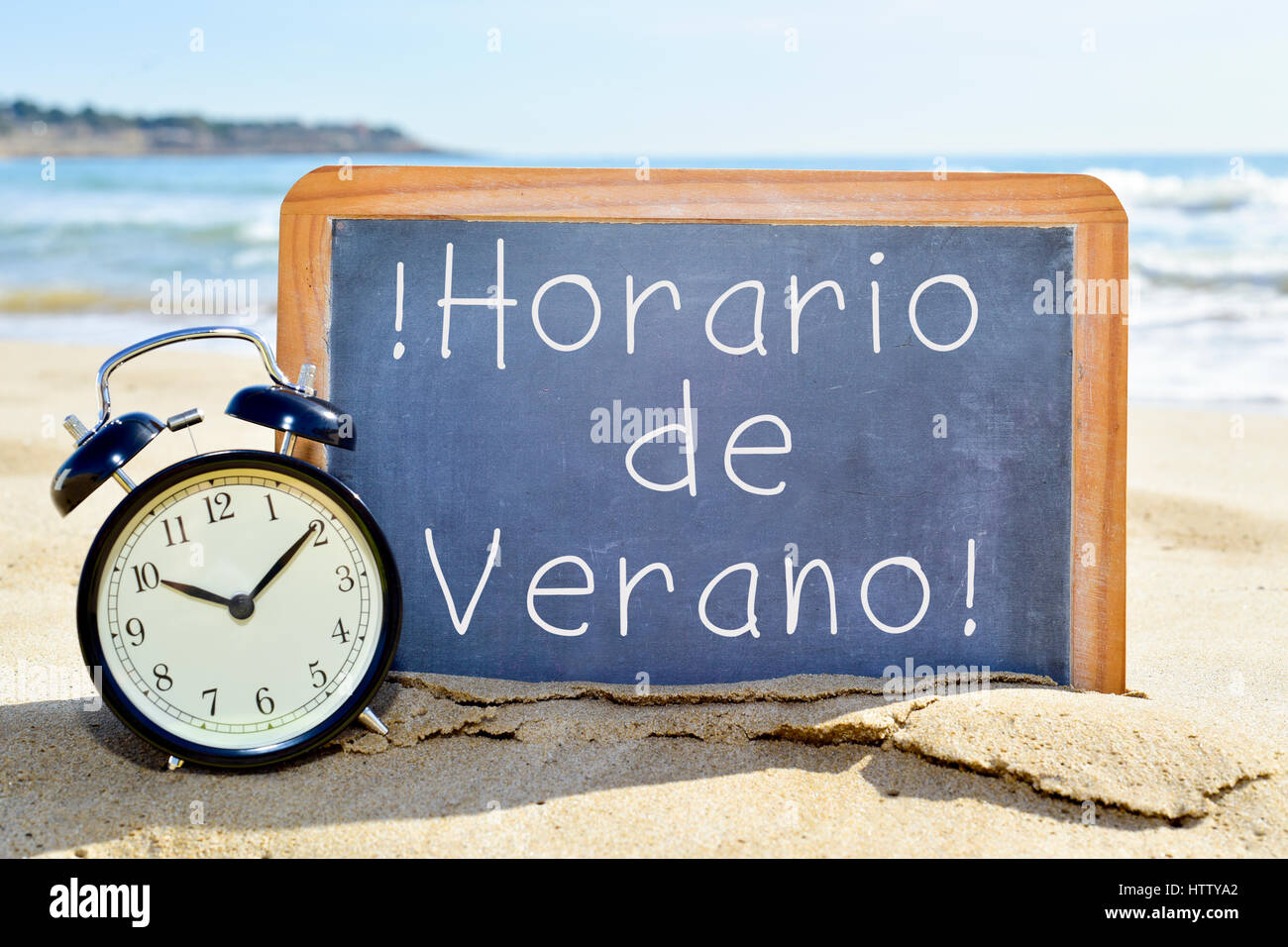 Un orologio di allarme e di una lavagna con il testo horario de verano, estate tempo in spagnolo, sulla sabbia di una spiaggia Foto Stock