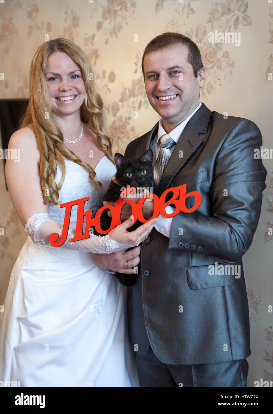 Felice e sorridente Caucasian giovane azienda red parola amore in russo in mano e gatto nero Foto Stock