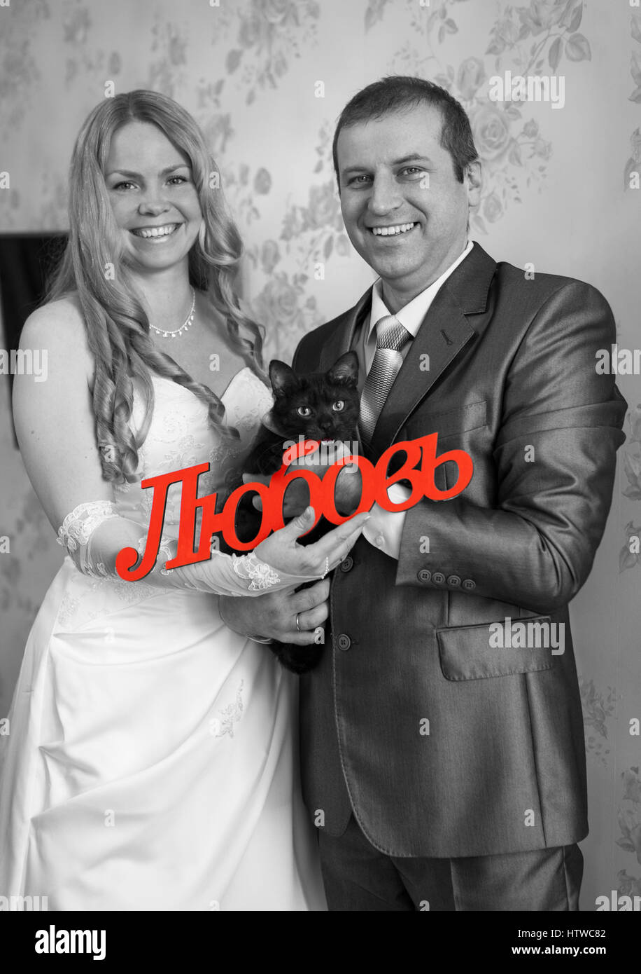 Felice e sorridente Caucasian giovane azienda red parola amore in russo in mano e gatto nero, immagine in scala di grigi Foto Stock