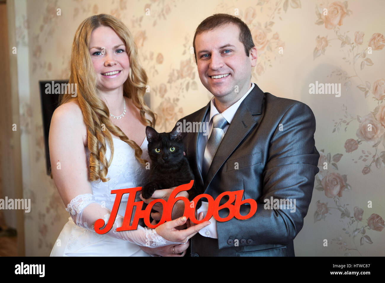 Gioioso matrimonio caucasico giovane azienda red parola amore in russo in mani e gatto nero Foto Stock