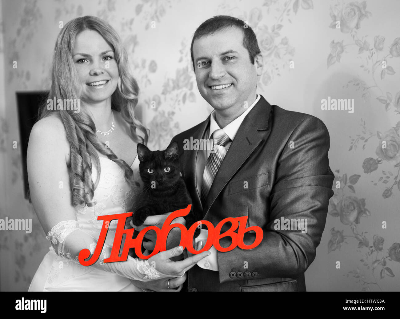 Gioioso matrimonio caucasico giovane azienda red parola amore in russo in mani e gatto nero, immagine in scala di grigi Foto Stock