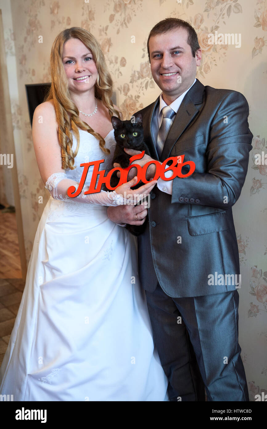 Gioiosa Caucasian coppie in viaggio di nozze con la parola amore in russo e il gatto nero è in stanza vuota Foto Stock