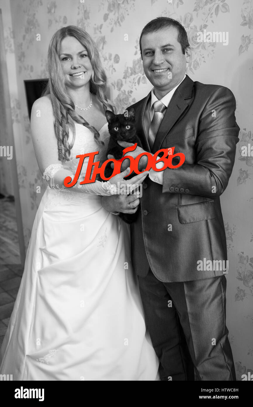 Gioiosa Caucasian coppie in viaggio di nozze con la parola amore in russo e il gatto nero è in stanza vuota, immagine in scala di grigi Foto Stock