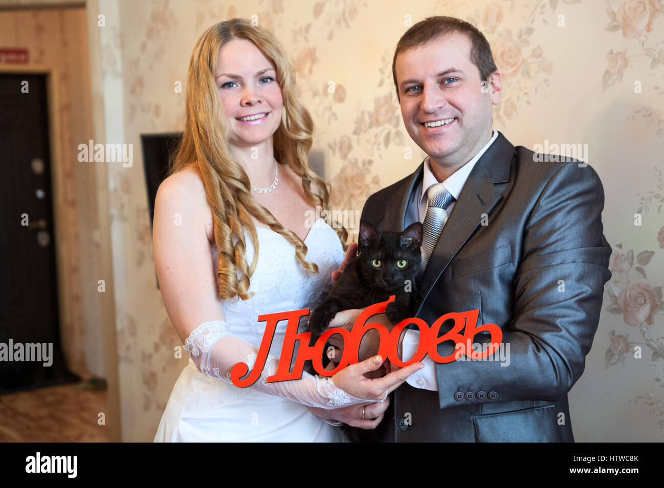 Caucasian sposa e lo sposo con gatto nero e la parola amore in russo in mani. Stanza vuota, inaugurazione della casa nuova Foto Stock