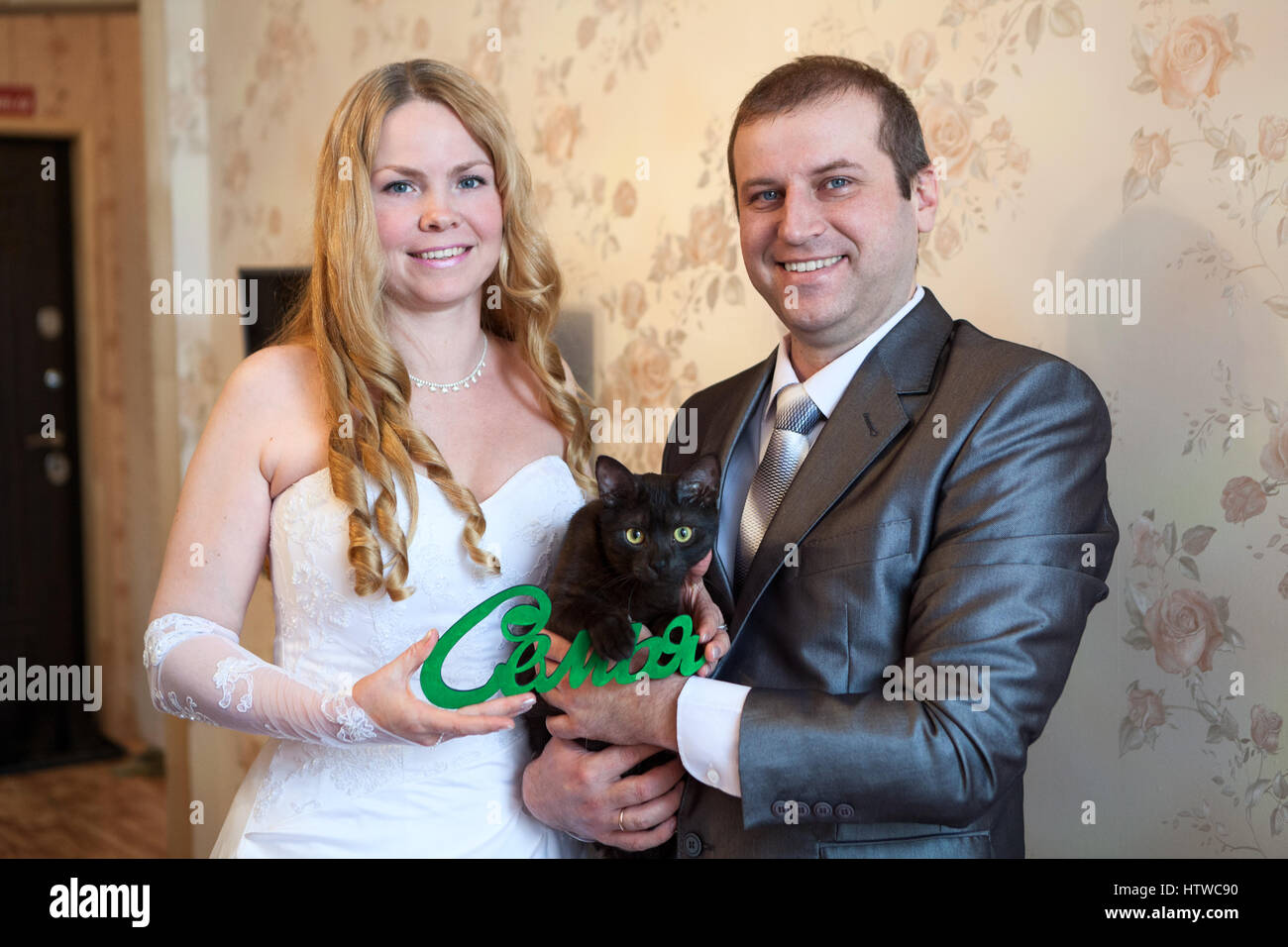 Felice e sorridente Caucasian giovane azienda red parola famiglia in russo in mani e gatto nero Foto Stock