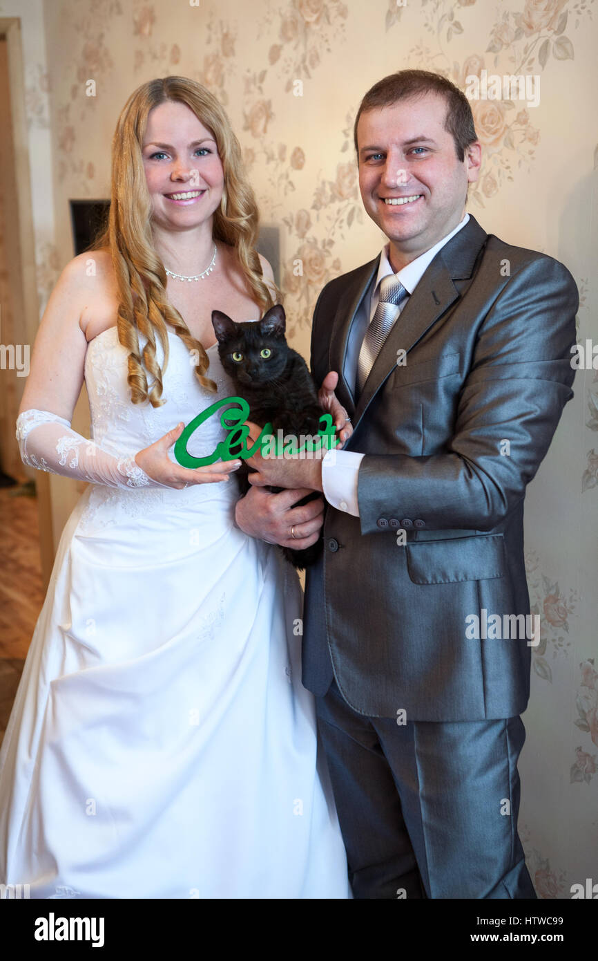 Gioiosa nozze caucasico giovane azienda green parola famiglia in russo in mani e gatto nero Foto Stock