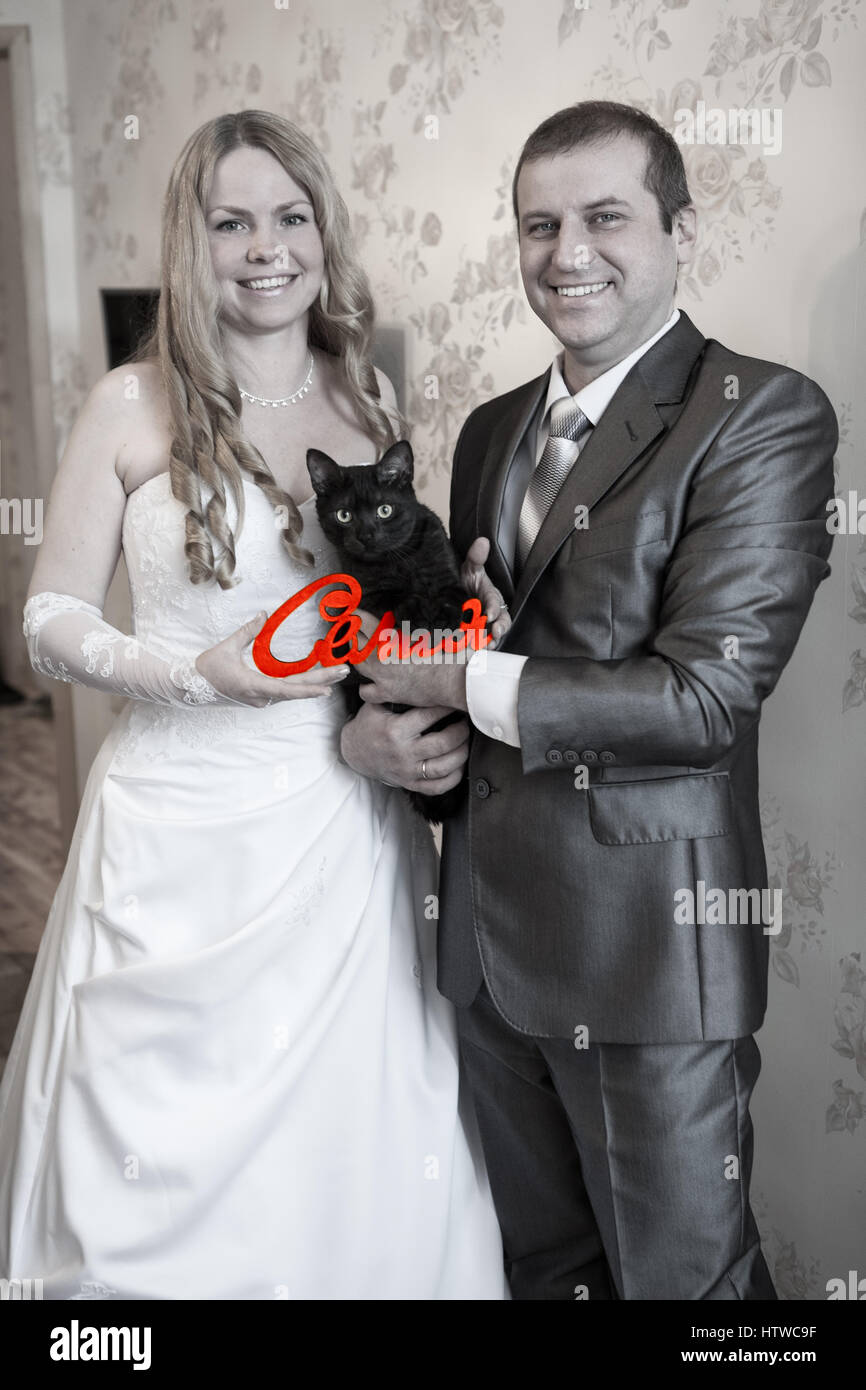 Gioiosa nozze caucasico giovane azienda green parola famiglia in russo in mani e gatto nero, immagine in scala di grigi Foto Stock