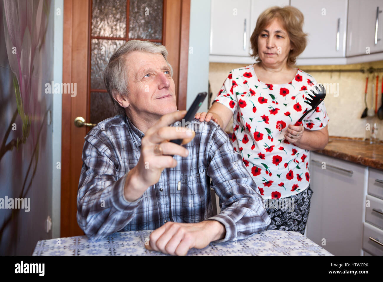 Moglie insoddisfatto con il marito l'ozio, un uomo commuta i canali con il telecomando di un televisore, cucina Foto Stock