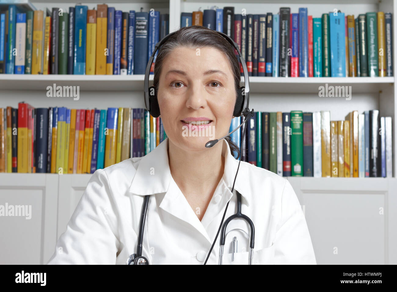 Medico o il medico di medicina generale con cuffia in chirurgia office parlare online con un paziente, come visto attraverso una webcam, concetto di telemedicina Foto Stock