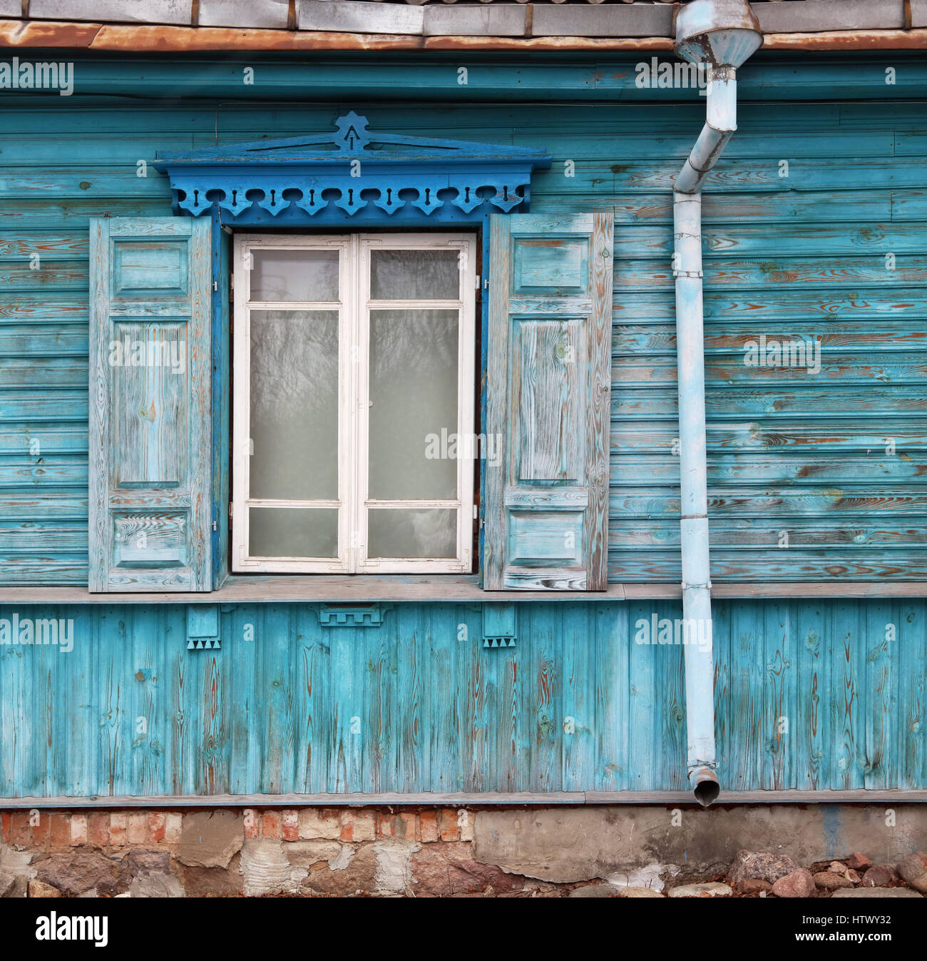 Finestre con apertura di tende da sole nel vecchio distrutto in legno di colore blu casa retrò. Pietra di granito base, rusty Il tetto e di un tubo di scarico Foto Stock
