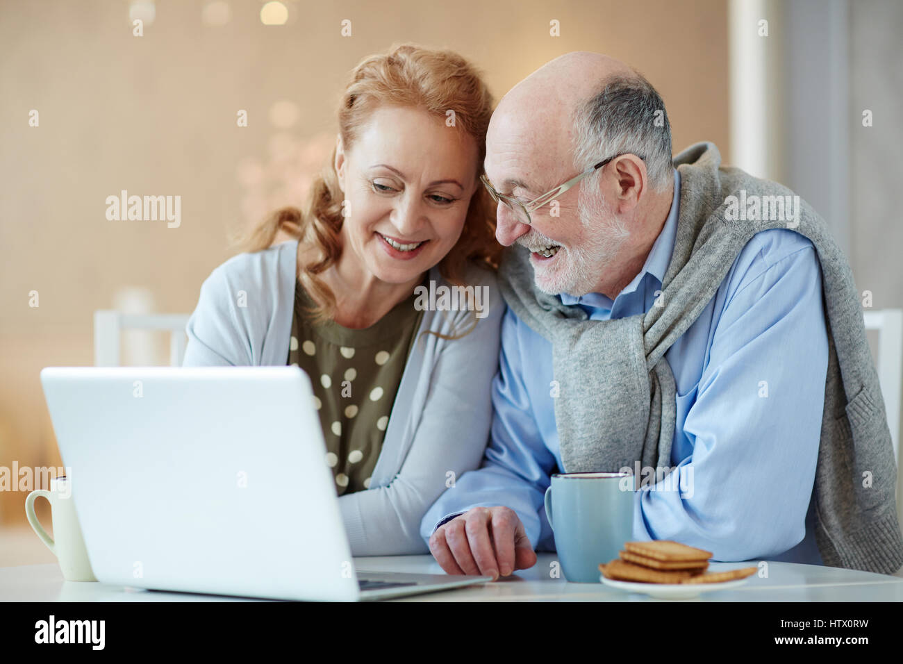 Ritratto di sorridente coppia di anziani, guardando curioso di imparare a utilizzare i moderni laptop home a tavola a ridere con gioia Foto Stock