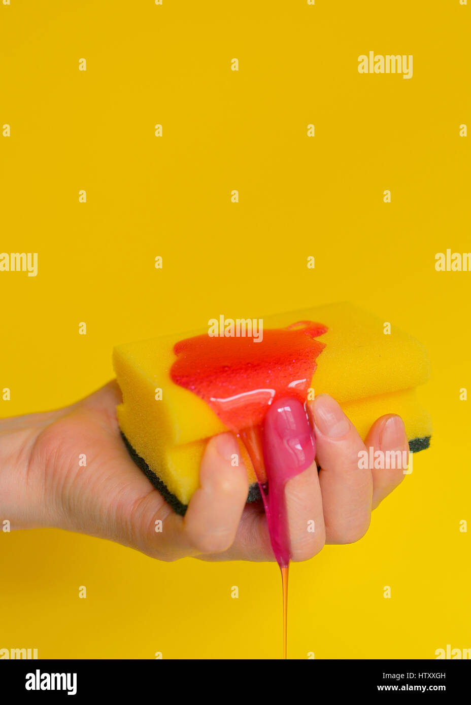 Mano con una spugna con schiuma su sfondo giallo Foto Stock