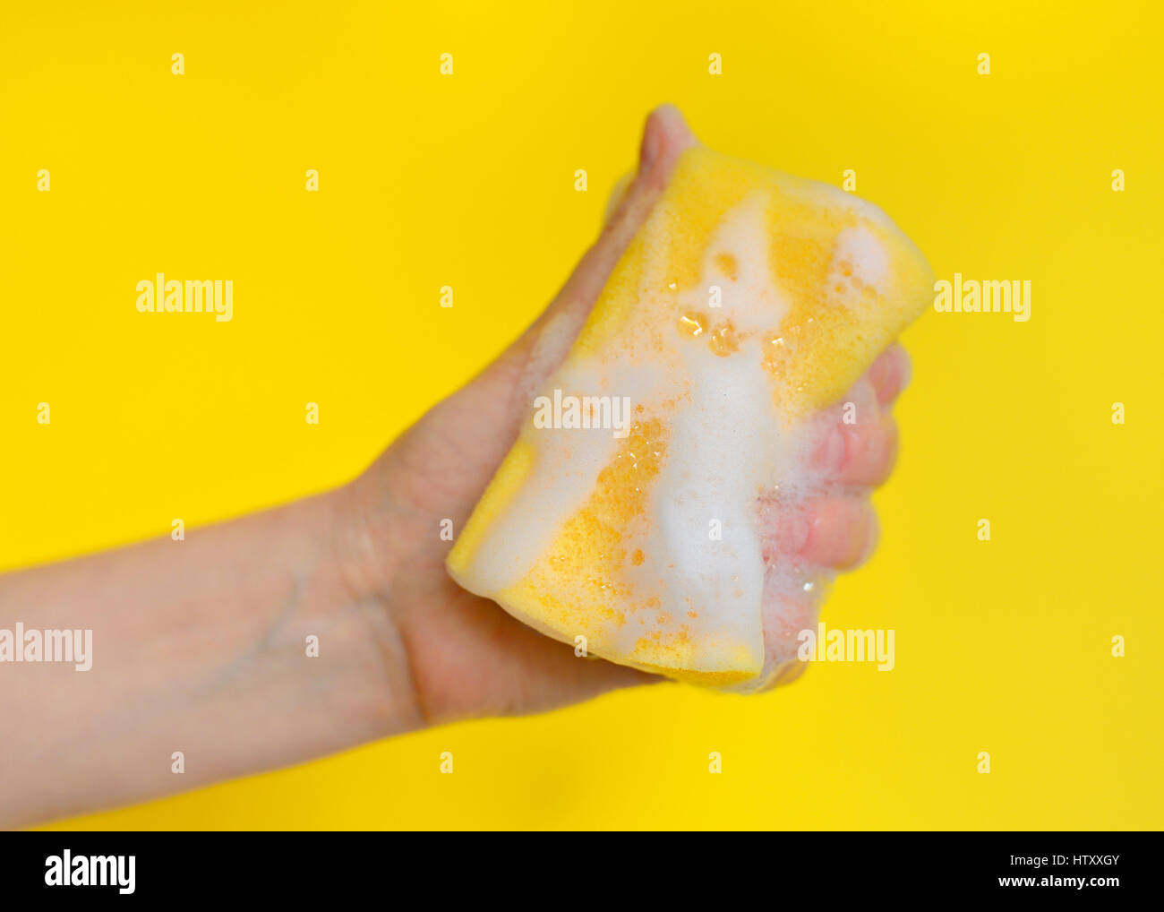 Mano con una spugna con schiuma su sfondo giallo Foto Stock
