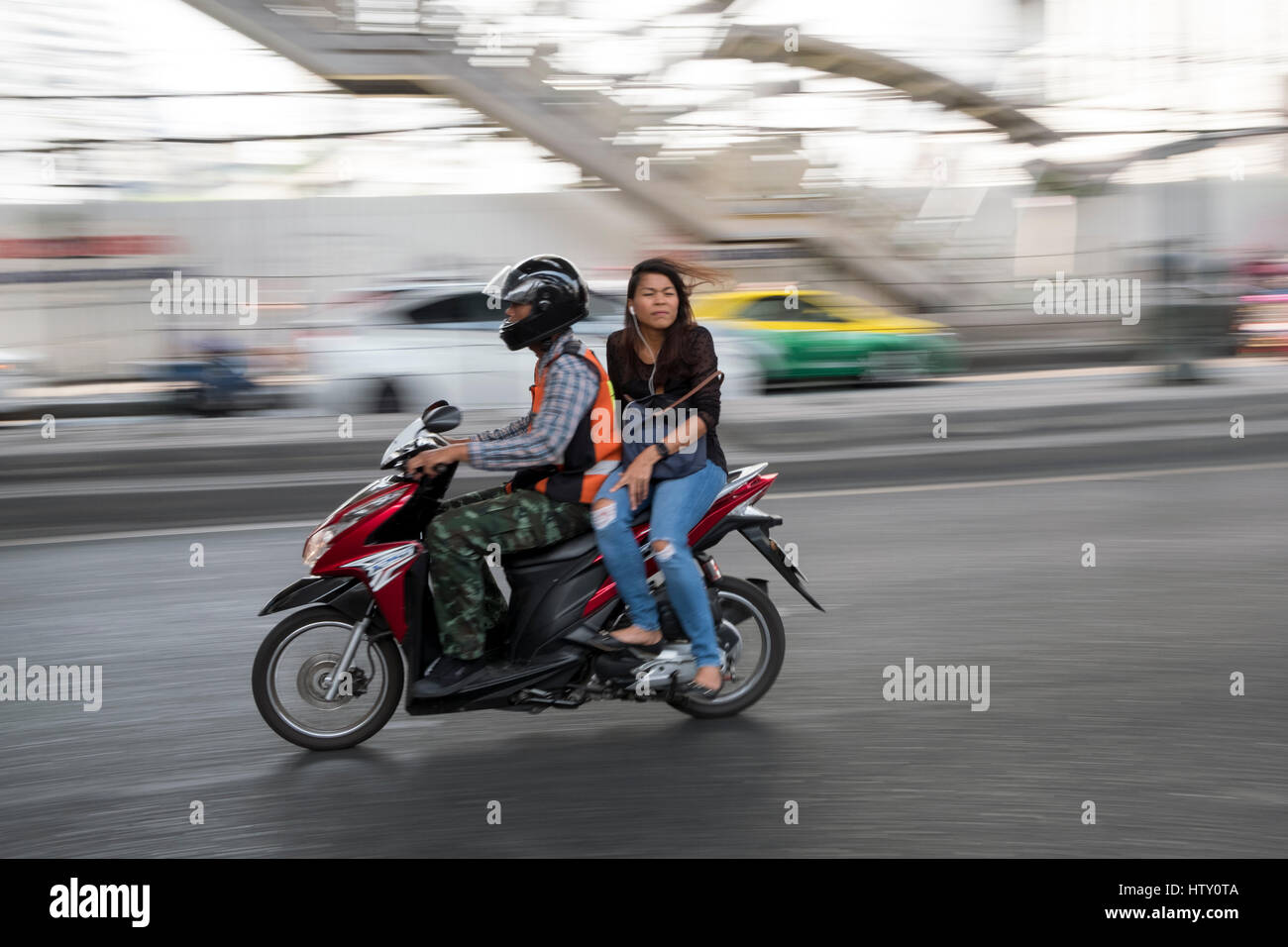 Un motociclista e passeggero velocità lungo Sukhumvit Road attraverso Sukhumvit Bangkok, Thailandia Foto Stock