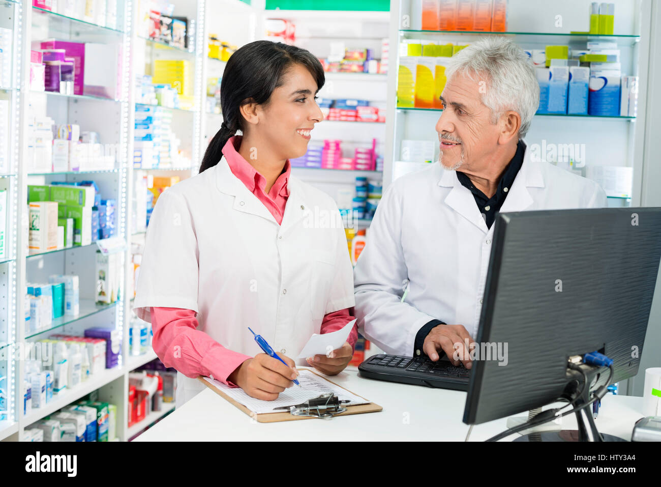 Il farmacista iscritto sulla clipboard mentre guardando il collega utilizzando co Foto Stock