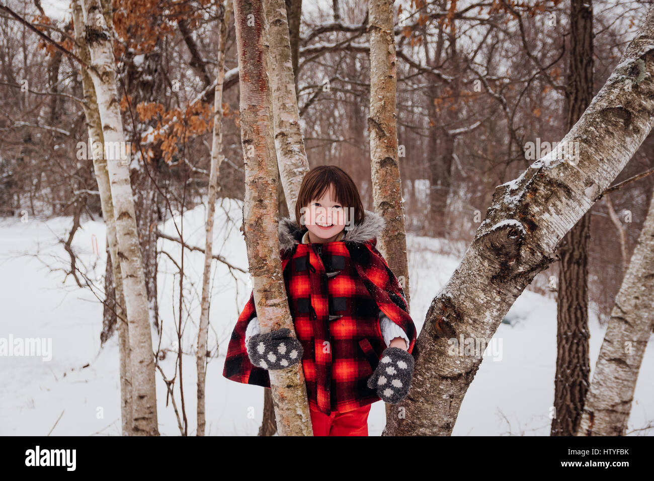 Ragazza in giacca con cappuccio in piedi tra gli alberi in inverno Foto Stock