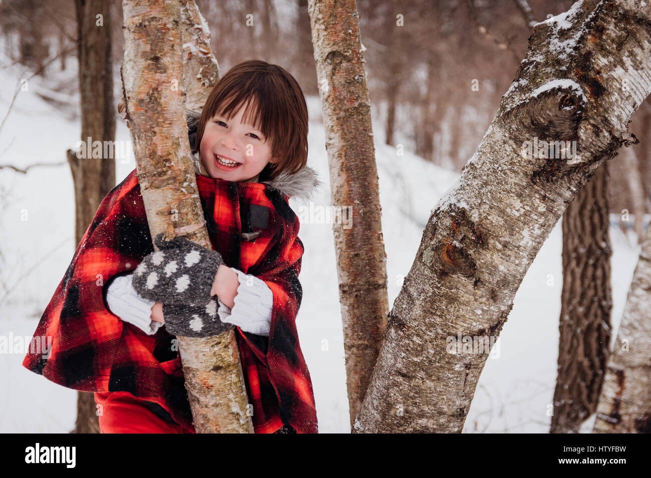Ragazza in giacca con cappuccio in piedi tra gli alberi in inverno Foto Stock