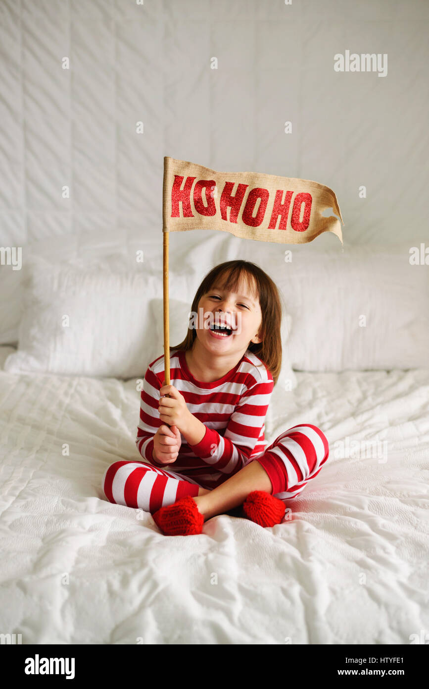 Ragazza seduta sul letto tenendo un HoHoHo bandiera Foto Stock