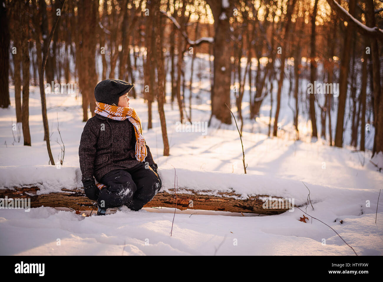 Ragazzo seduto su un registro nel bosco in inverno Foto Stock