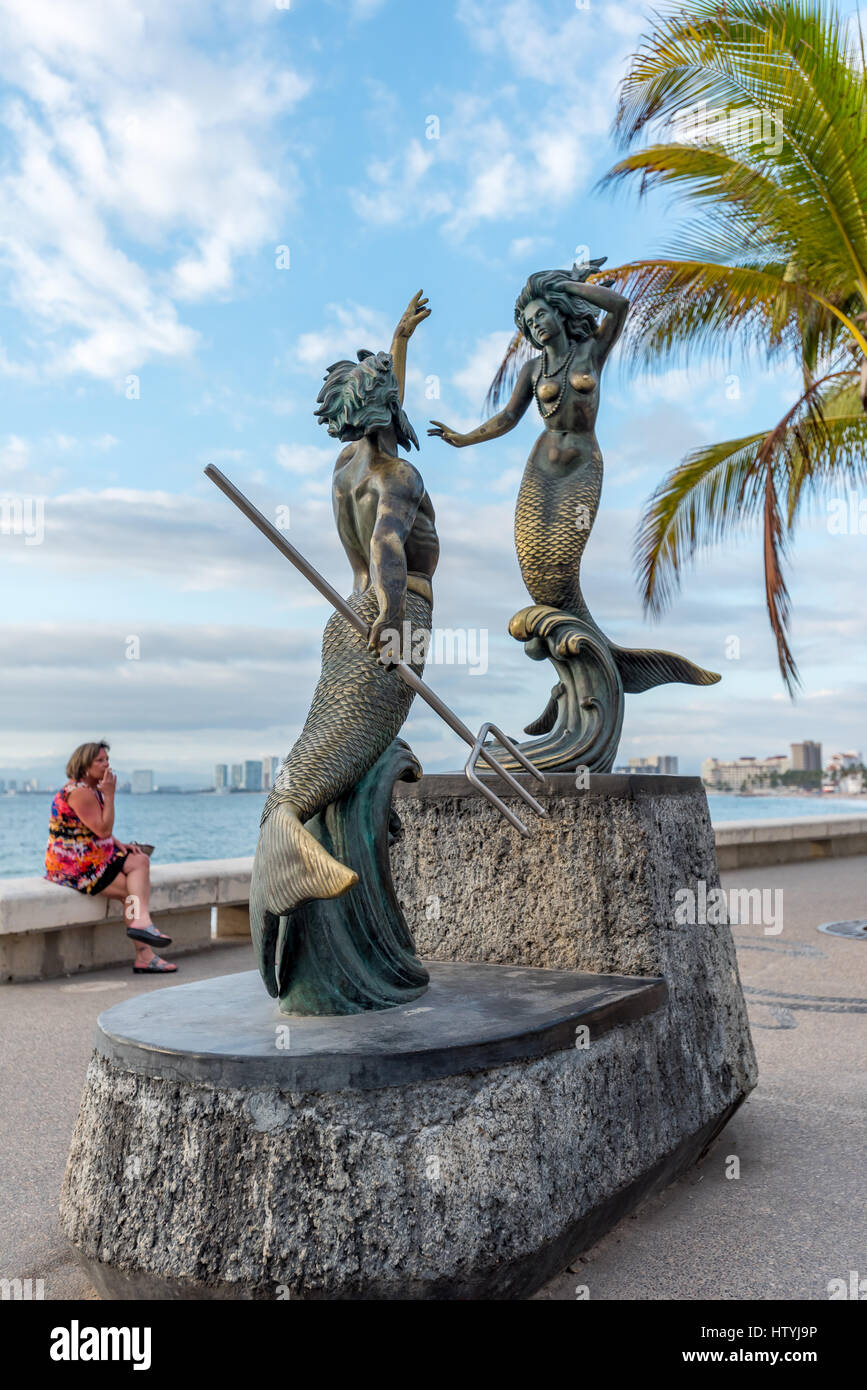 Scultura di Triton e sirena da Carlos Espino (Nettuno e la nereide) su Puerto Vallarta Malecon w/ donna in background indossando abiti colorati Foto Stock