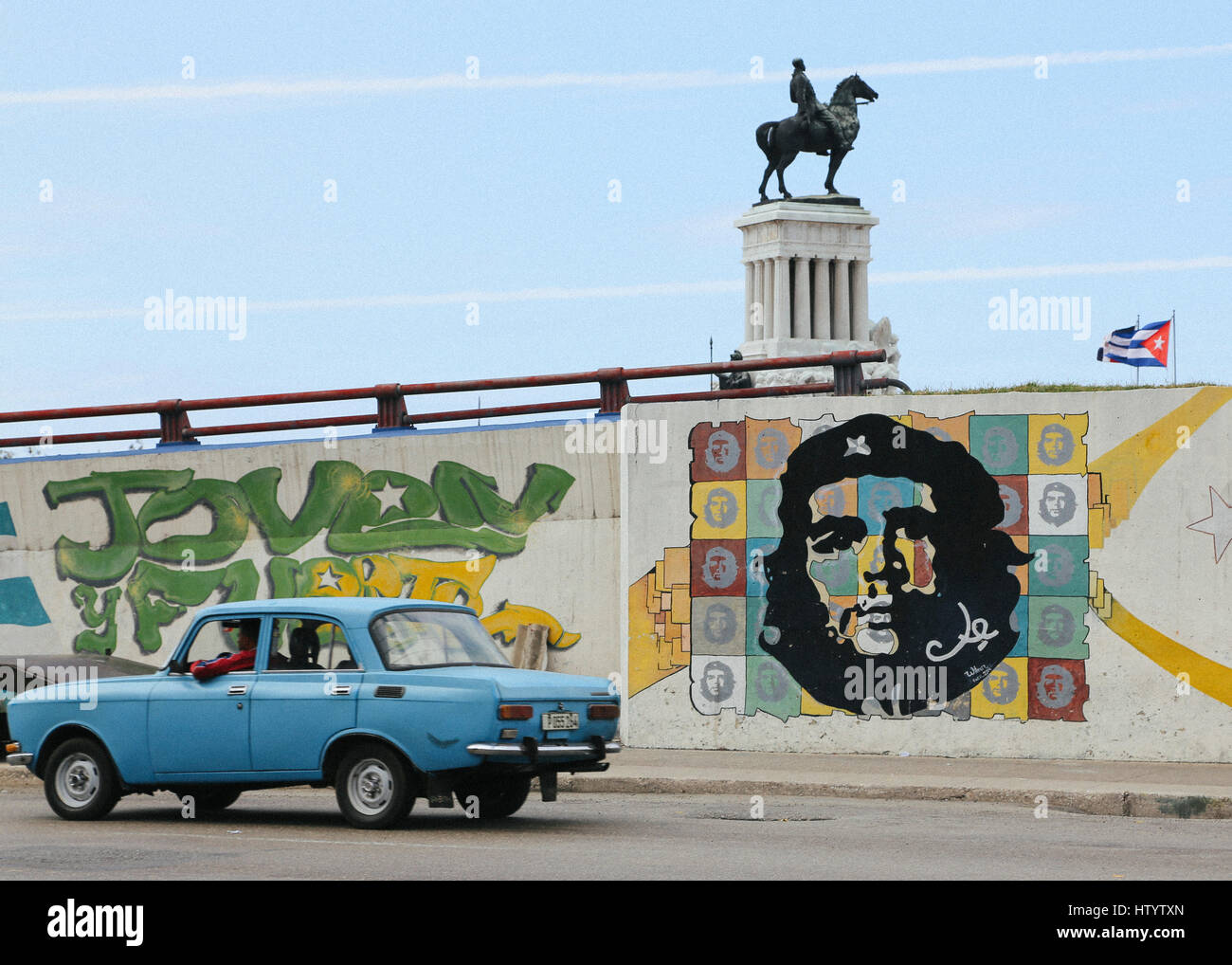 Un vecchio blu Lada Automobile visto sulla strada dal monumento di Maximo Gomez e arte di strada raffiguranti Che Guevara in Havana, Cuba Foto Stock