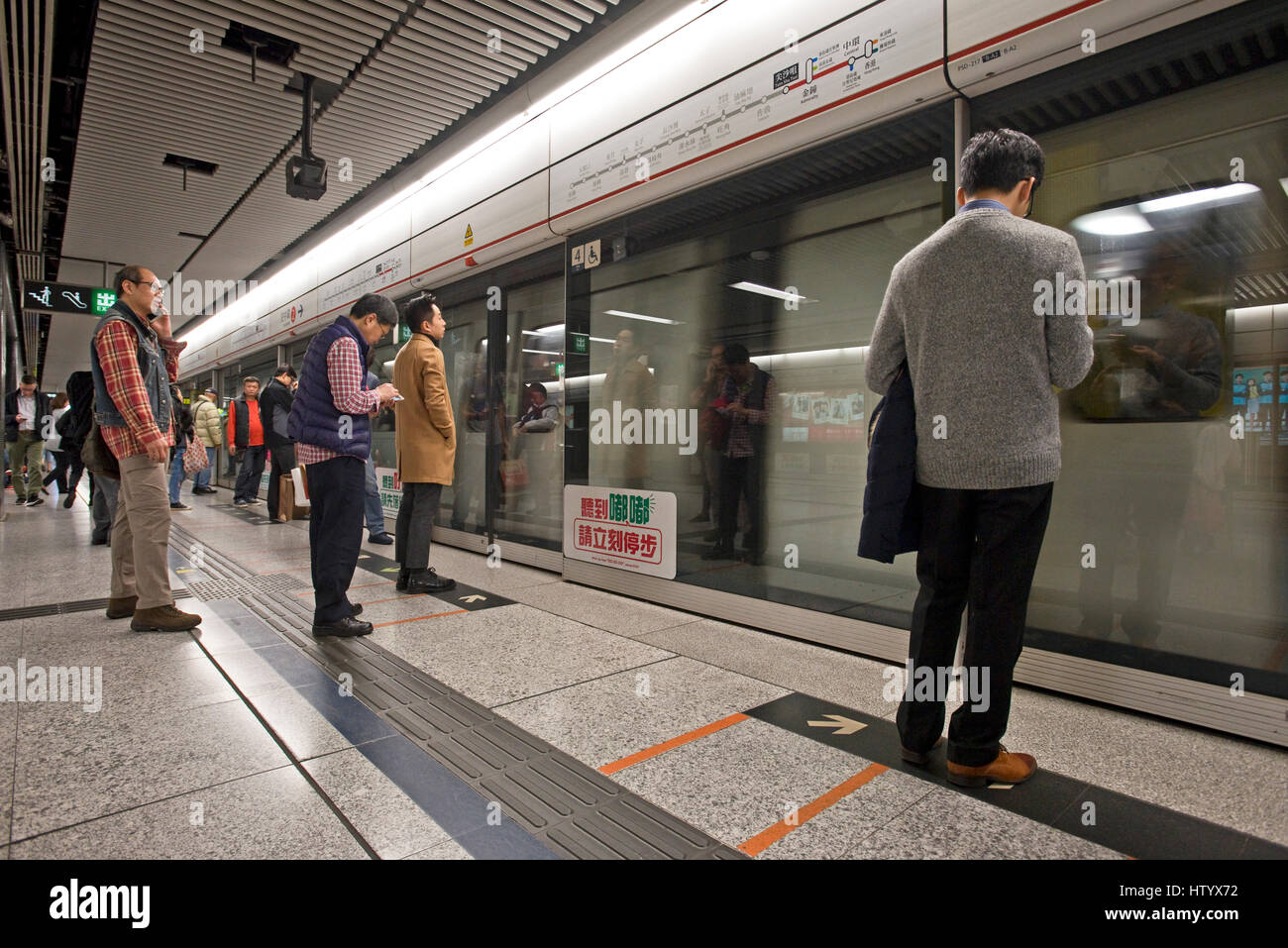 Pendolari in attesa in piedi su una piattaforma sul sistema MTR di Hong Kong come un treno tira in alla stazione. Foto Stock