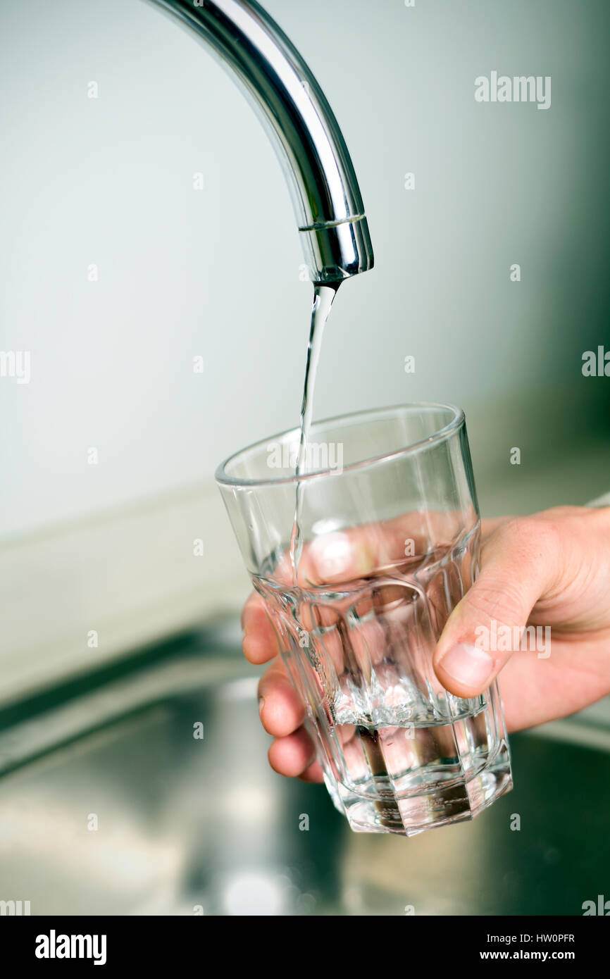 Primo piano di un giovane uomo caucasico riempire un bicchiere di acqua di rubinetto da un rubinetto con un piccolo flusso di acqua Foto Stock