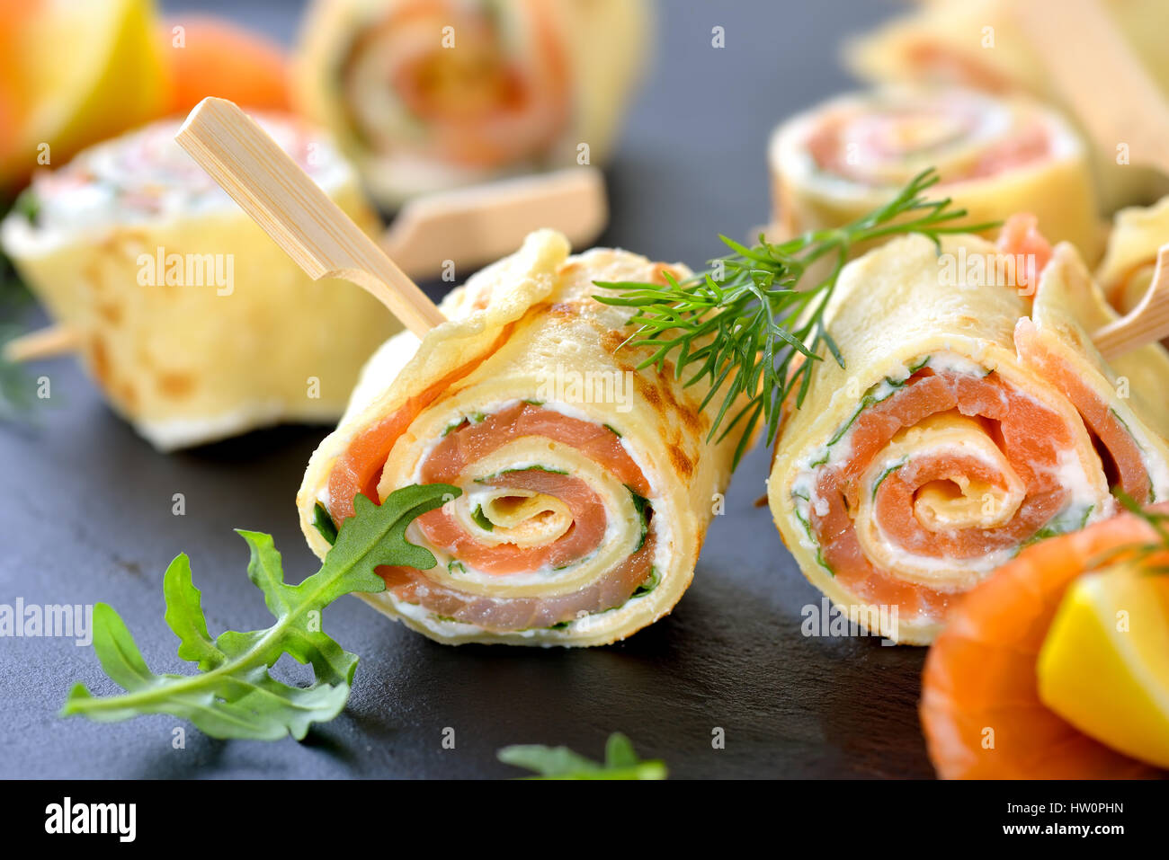 Rotoli di sottili frittelle con salmone affumicato, il rafano crema di formaggio e rucola Foto Stock