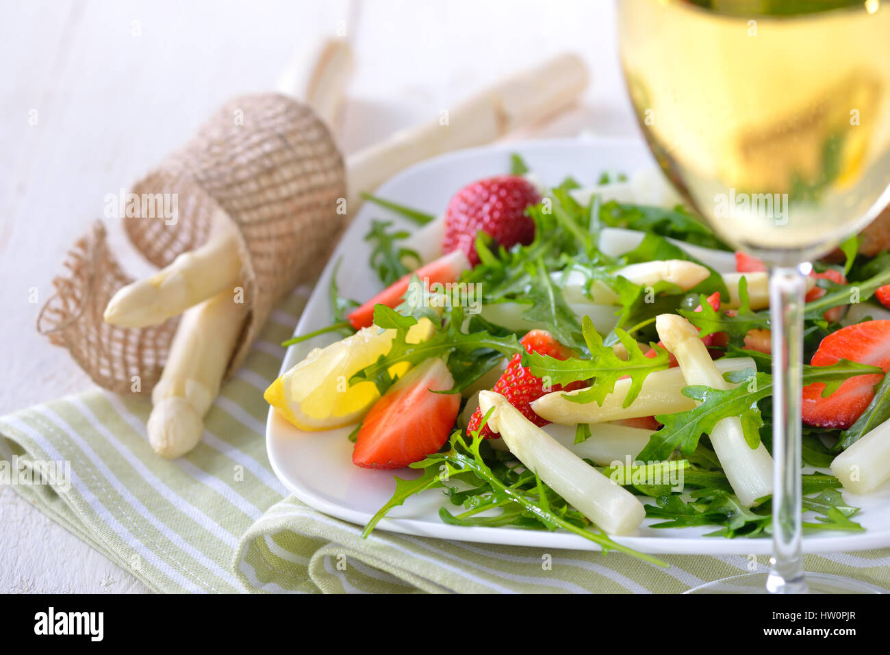 Colorato con insalata primavera con freschi Asparagi bianchi, insalata di rucola e fragole, servito con un bicchiere di secco e fruttato Vino bianco Foto Stock