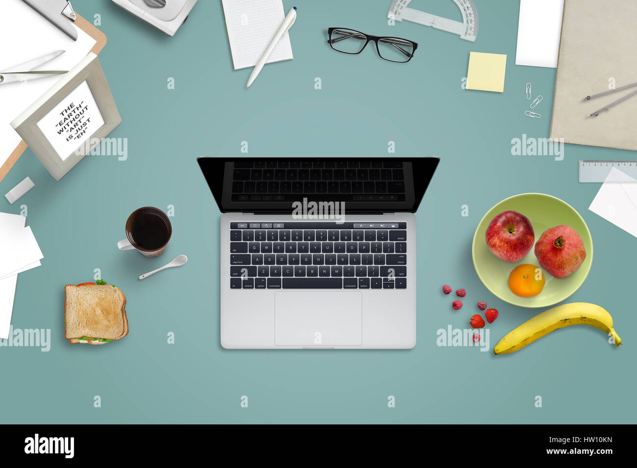 Laptop e cibo circondato da forniture di ufficio. Il duro lavoro in ufficio e rompere con frutta fresca e un panino.Vista dall'alto. Foto Stock