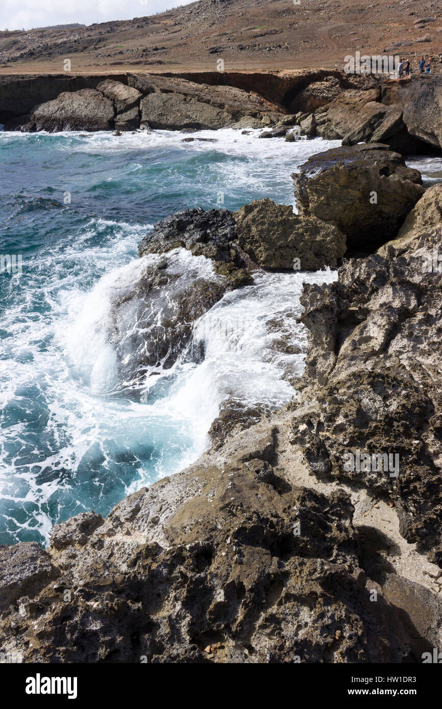 Le acque azzurre del Mar dei Caraibi crash sulla North Shore di Aruba con il crollo del ponte naturale in background. Foto Stock