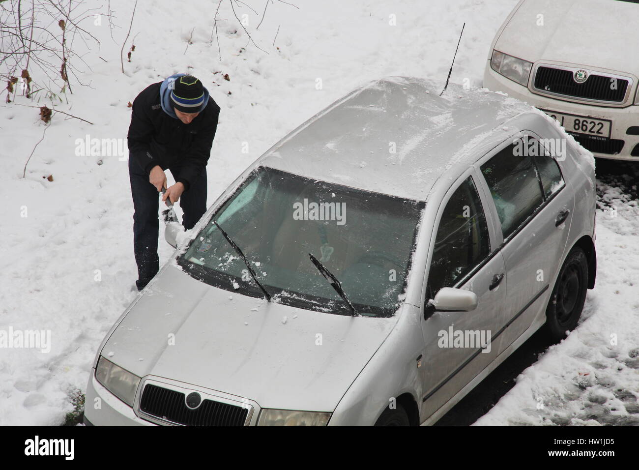 Il proprietario di un'autovettura in Praga area Libeň raschia fuori la neve e il gelo sul suo veicolo al fine di essere in grado di estrarre la sua auto parcheggiata. Foto Stock