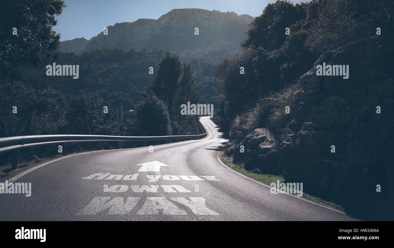 Lunga strada deserta attraverso le montagne con parole di trovare la propria strada e freccia su asfalto Foto Stock