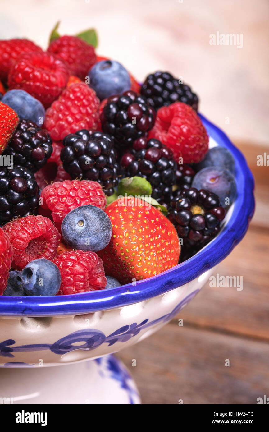 Frutta estiva in blu e con frutta in ceramica ciotola, con una selezione di mirtilli, lamponi, fragole e more. Foto Stock