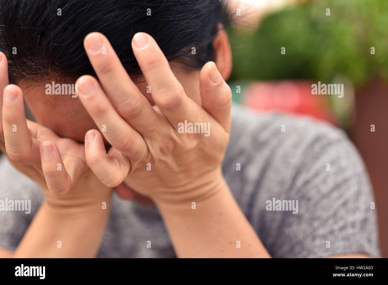 Giovane donna attraente nasconde il suo volto nel palmo delle sue mani vestito casualmente. Foto Stock