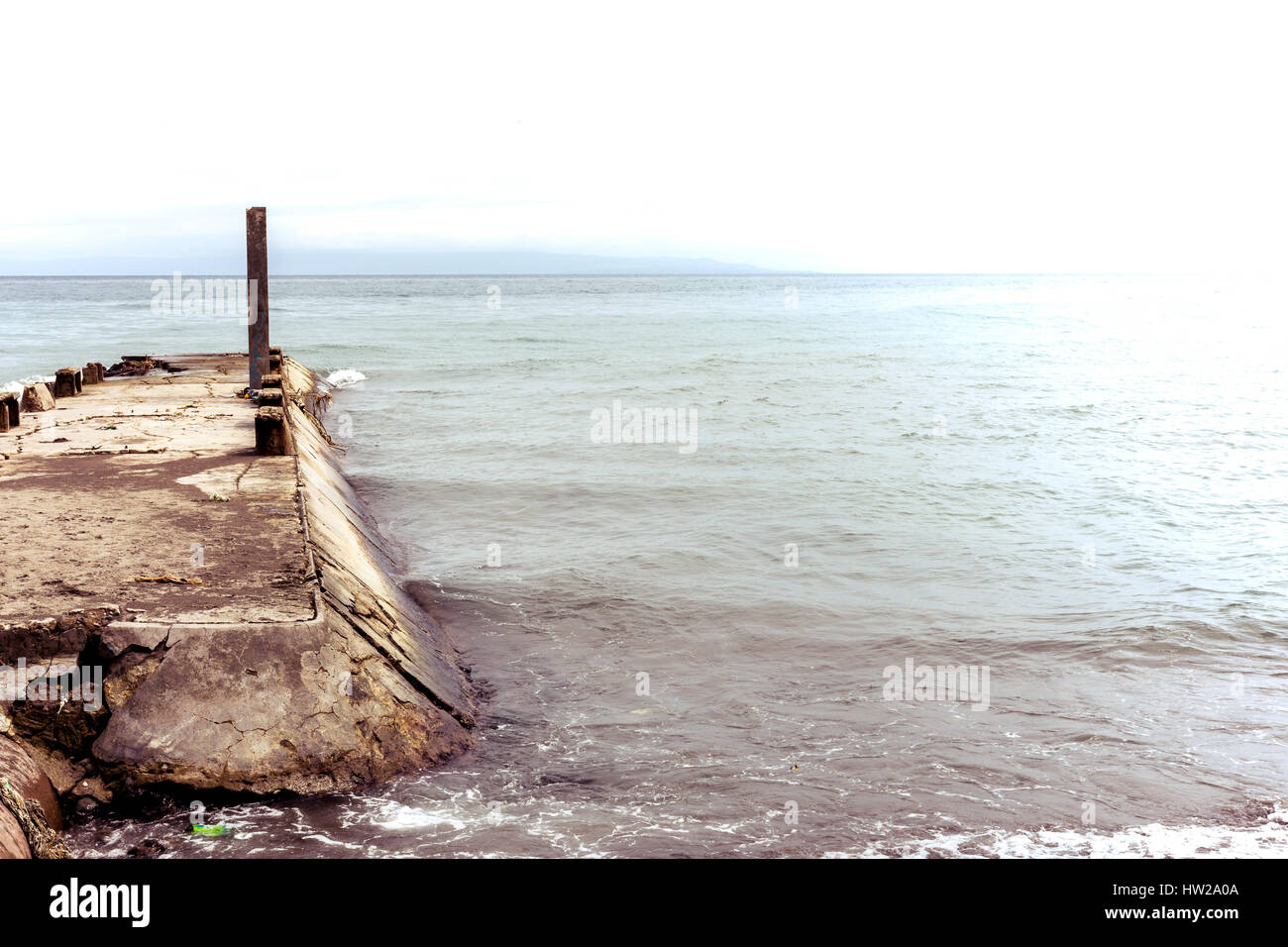 Vecchio cemento jetty pier in necessità di riparazione si protende in un mare calmo con sopra esposti effetto. Foto Stock