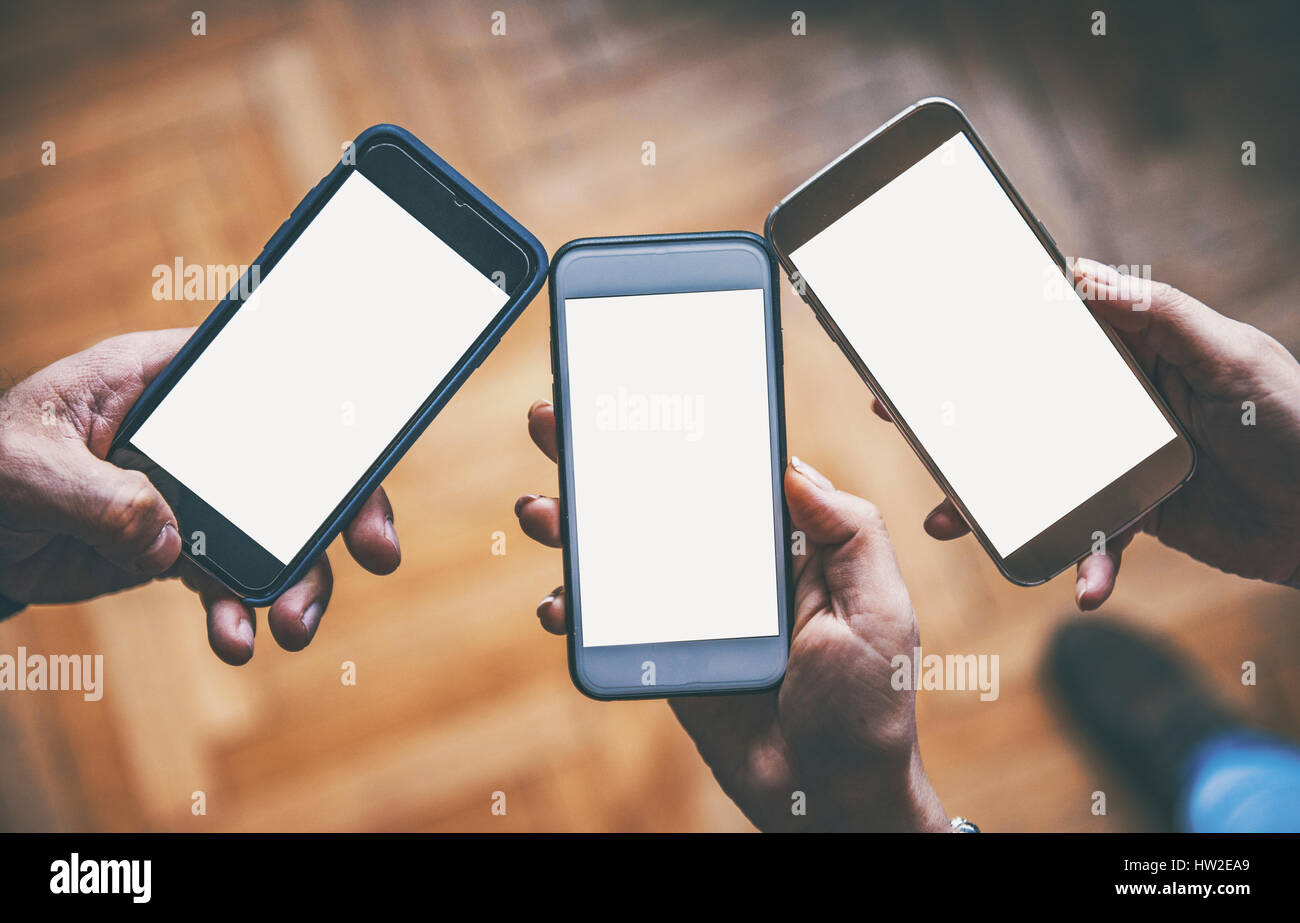 Tre mani tenendo i telefoni intelligenti Foto Stock