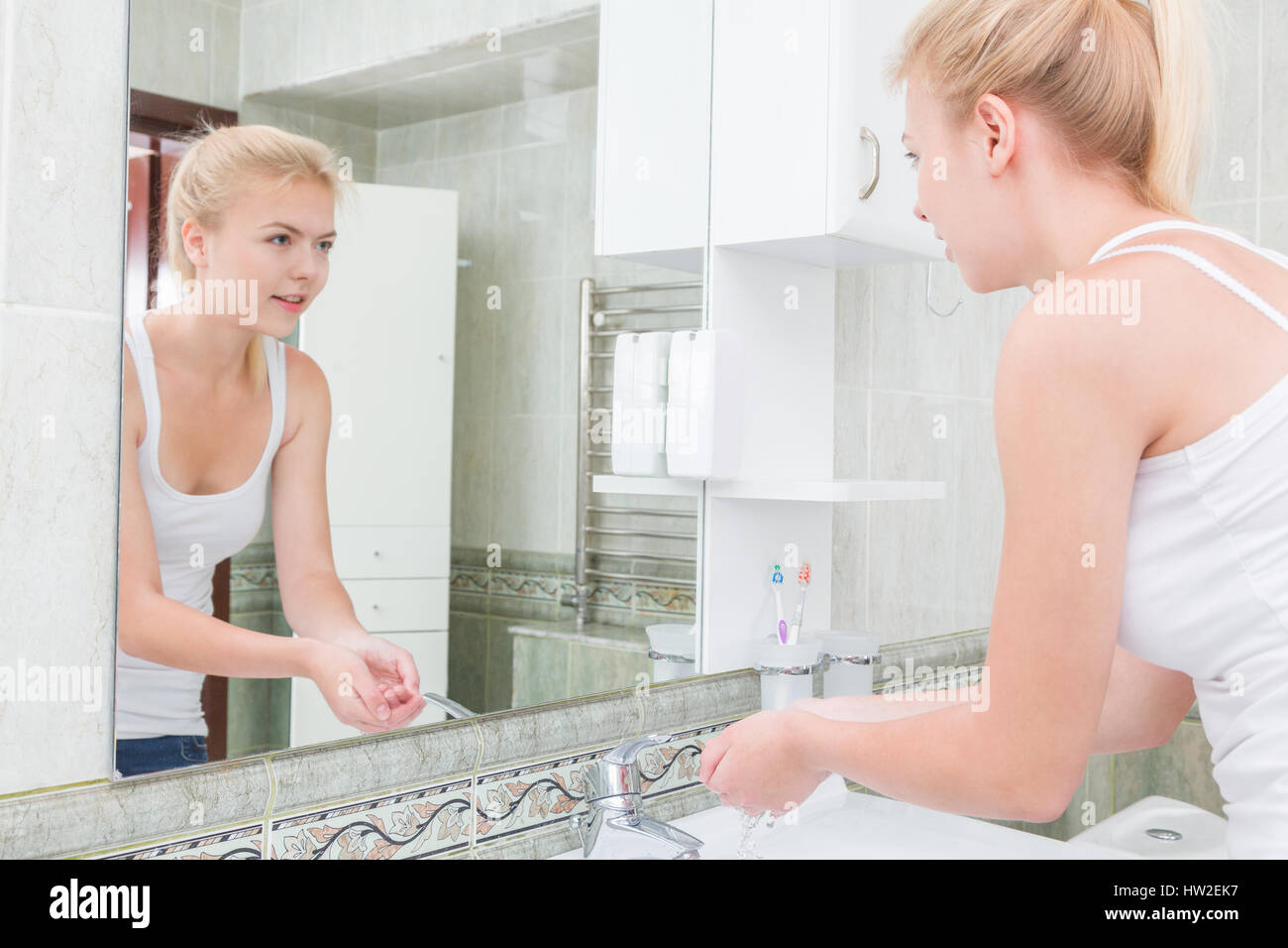 Giovane donna lavando le mani e il viso con acqua pulita in bagno Foto Stock