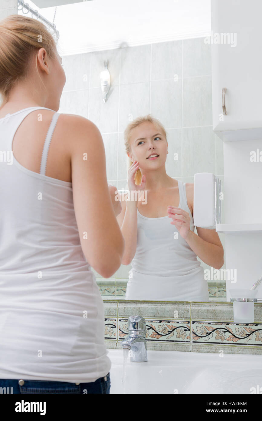 Giovane donna lavando le mani e il viso con acqua pulita in bagno Foto Stock
