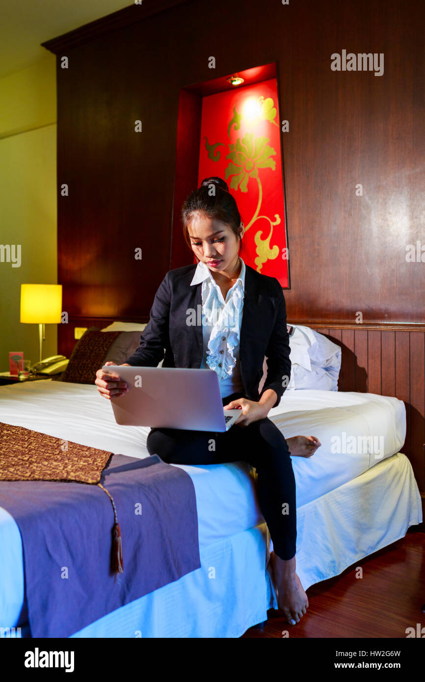 Asian imprenditrice seduta sul letto hotel utilizzando laptop Foto Stock