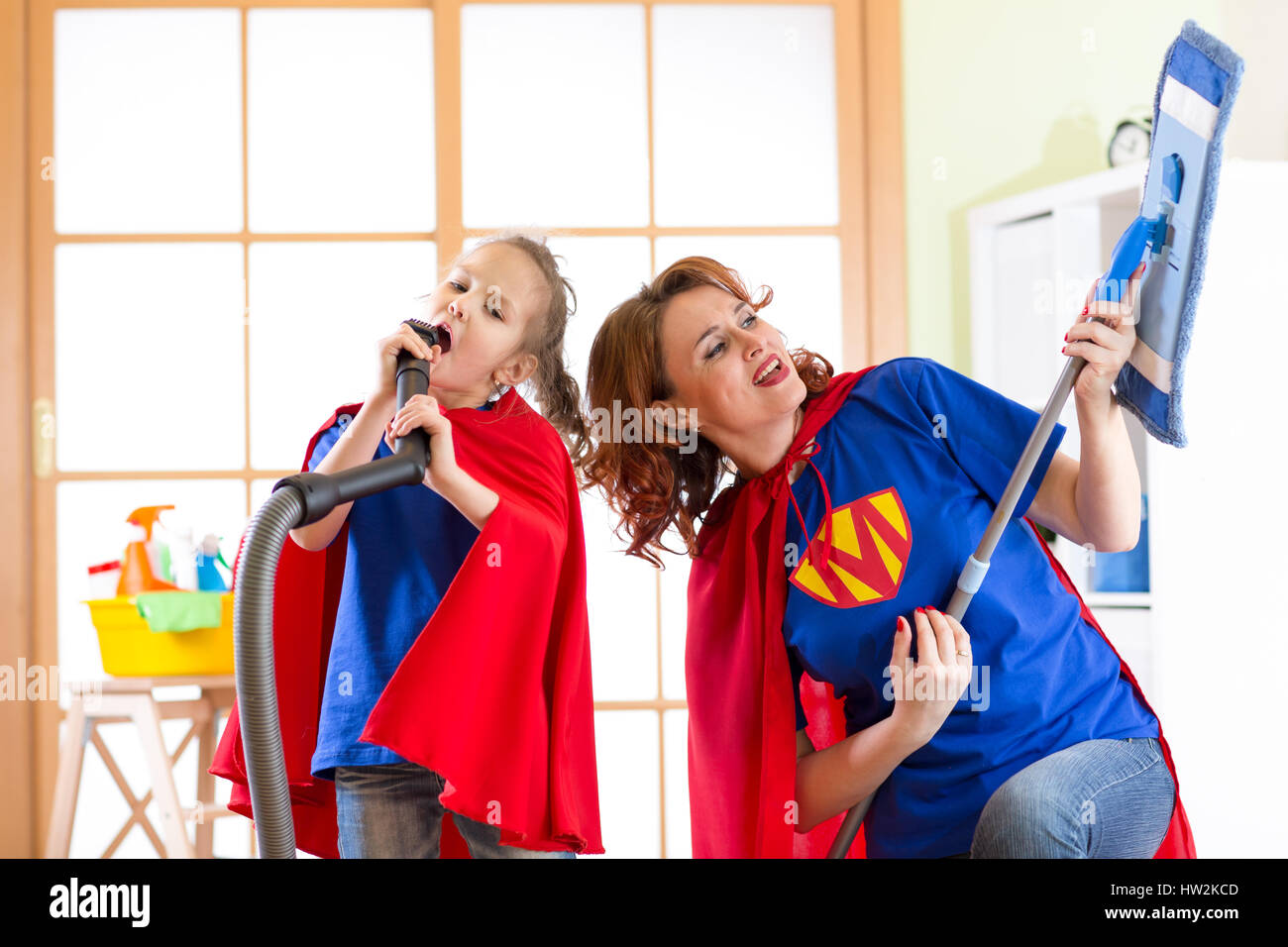 Preschooler ragazza e la sua madre vestita come supereroi. Donna di mezza età e kid giocare mentre si esegue la pulitura a casa Foto Stock
