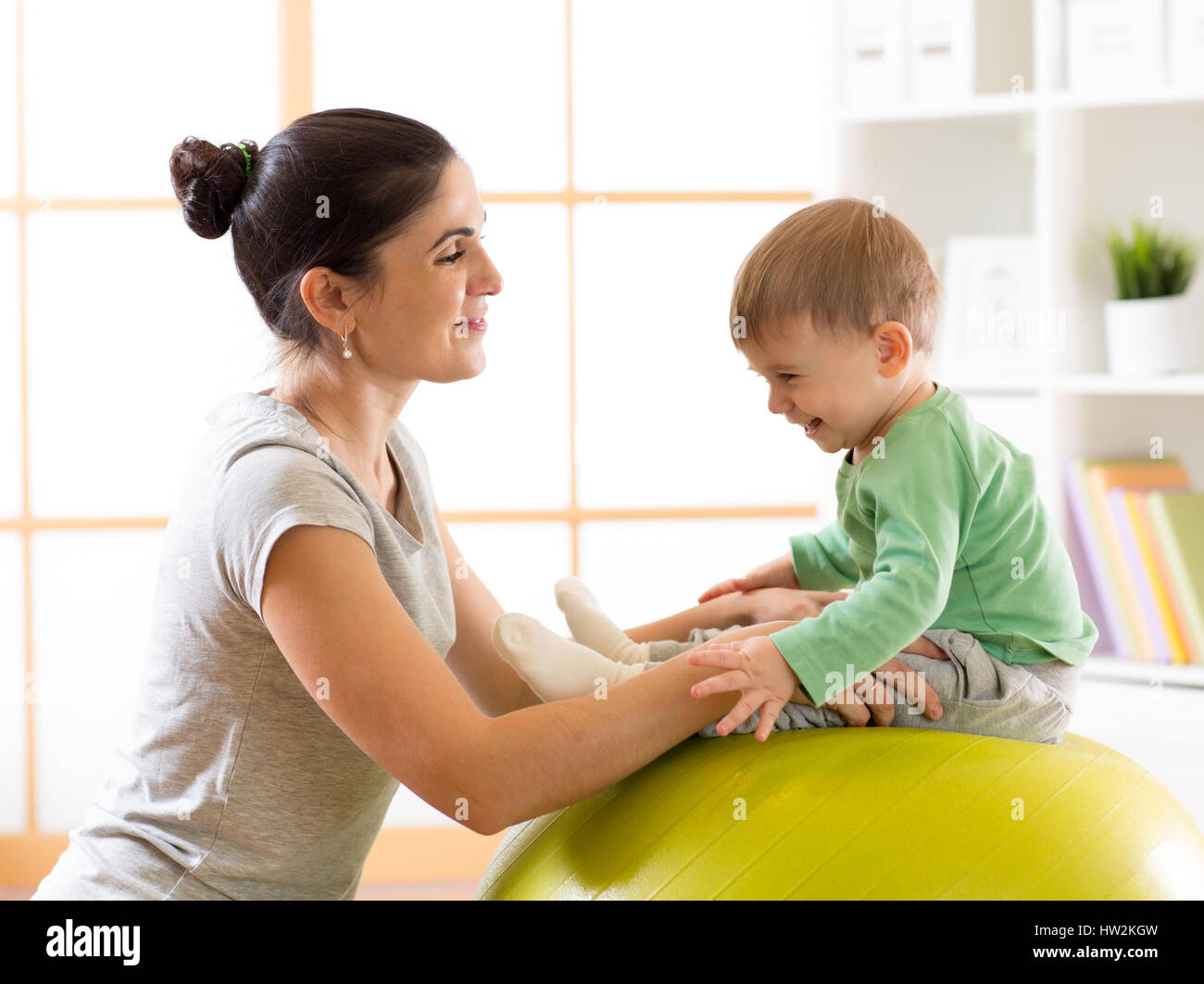 Felice madre con bambino facendo ginnastica sulla grande sfera di fitness in palestra Foto Stock