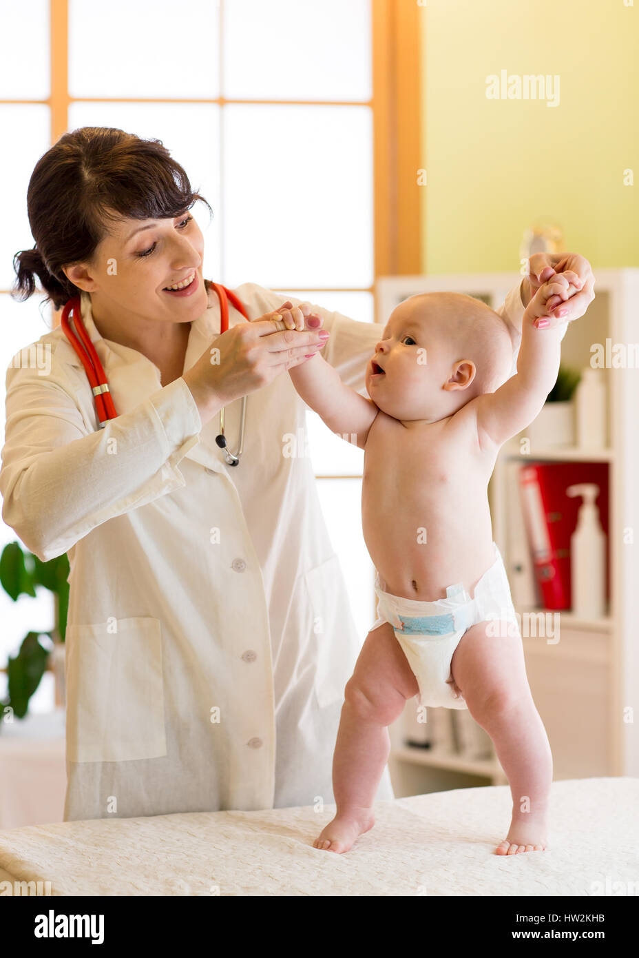 Felice simpatico baby a salute esame presso l'ufficio del medico. Pediatra supporta il neonato bambino mentre si sta in piedi Foto Stock